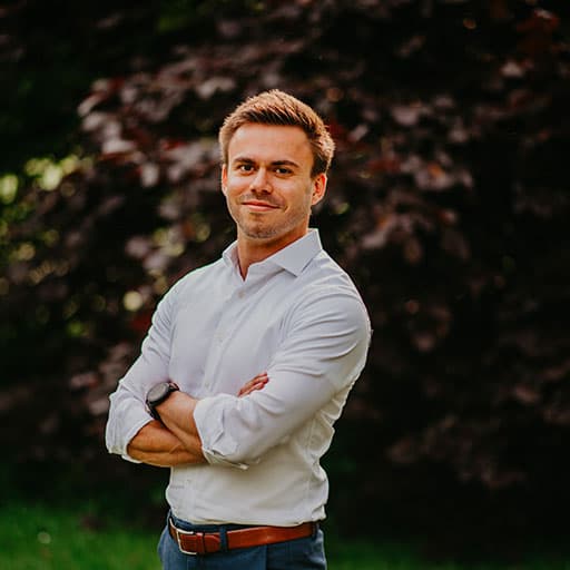 Tom standing confidently with arms crossed, facing the camera, on a landing page background.